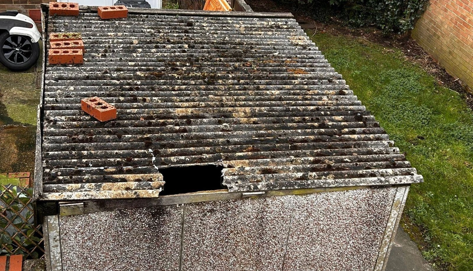 Old garage roof with broken asbestos sheet and moss damage
